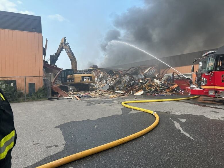 A fire truck sprays water on smoking rubble beside a large building.