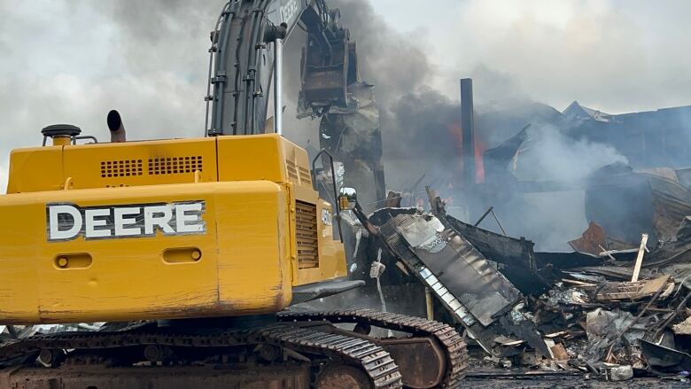 A building on fire, an excavator clearing debris.