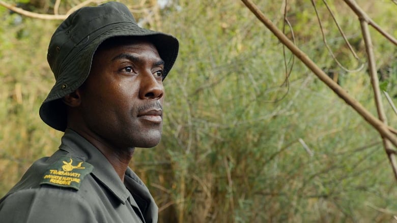 Side profile of a man's head and shoulders. He is wearing a bucket hat and matching olive uniform.