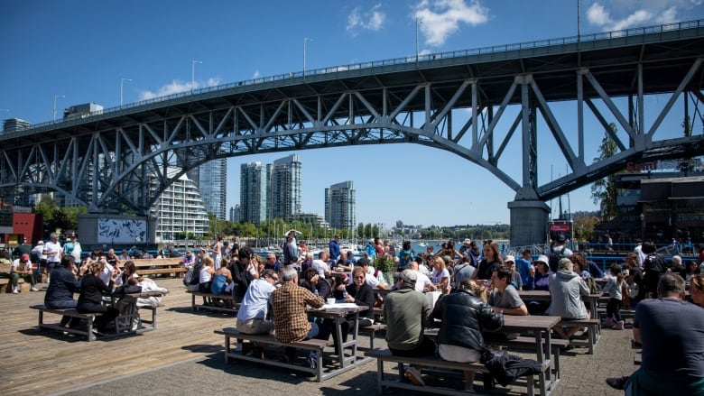 People sit on Granville Island as the bridge looms over their heads.