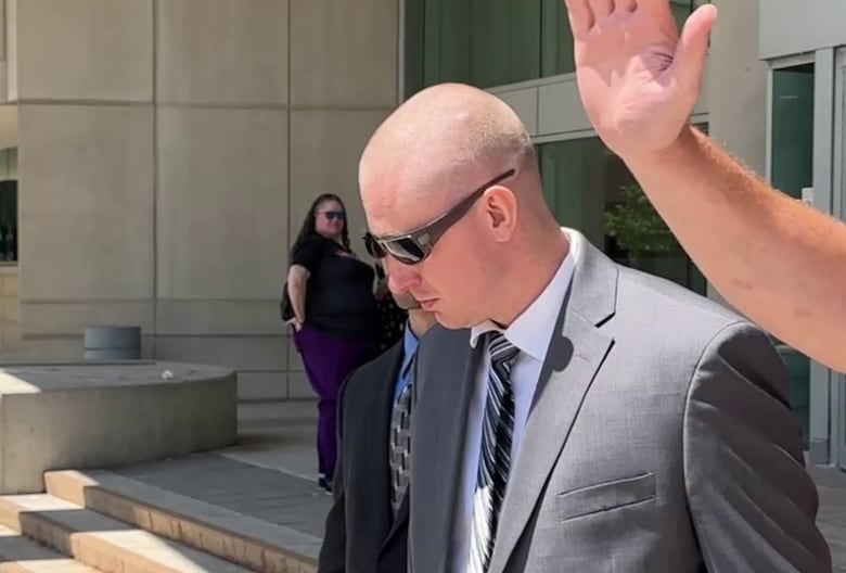 A man in a suit wearing sunglasses leaves a courthouse.