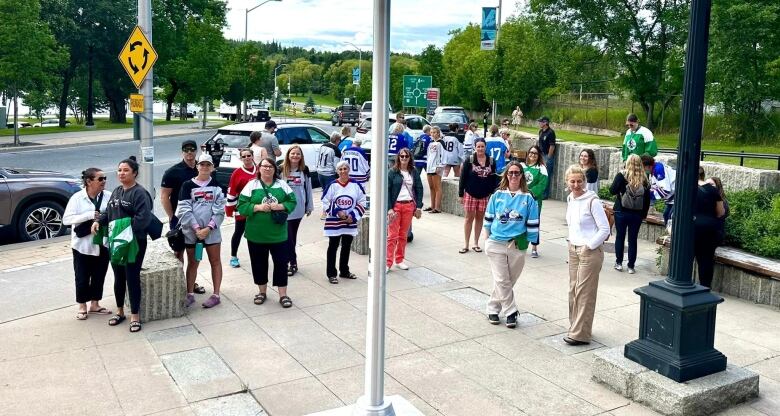 A group of people is seen standing outside. Many of them are wearing hockey jerseys.