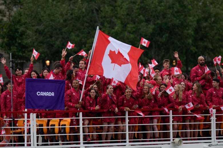 Canadian athletes in red gear celebrate in a boat as they participate in the Olympics opening ceremony.