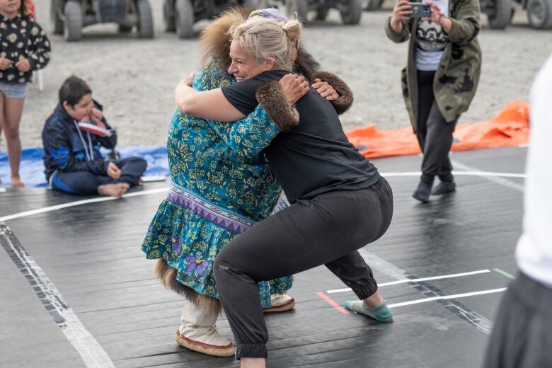 A blond woman in her 30s wrestles with an Inuit elder woman