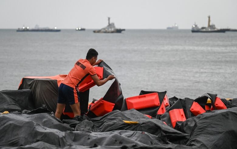 A coast guard member arranges an oil spill containment boom at a port.