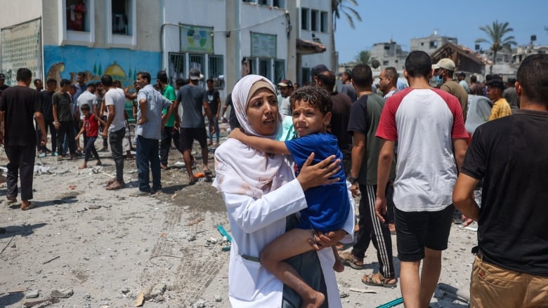 A woman holds a child as they navigate through a crowd.