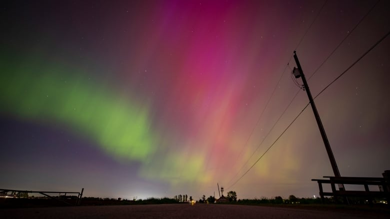 A sky is lit up by red and green lights from the aurora borealis.