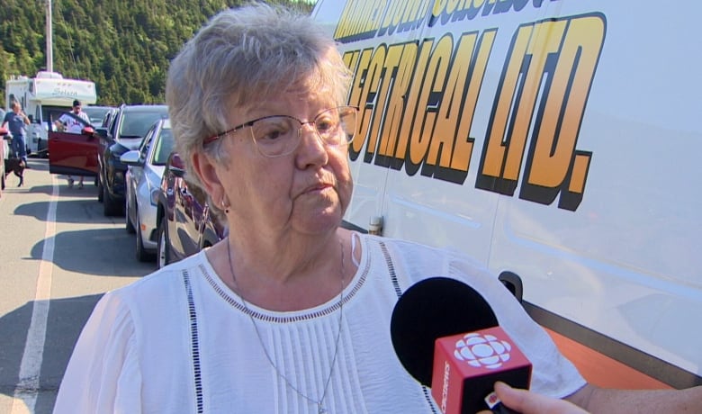 Older woman in white shirt stands by truck. 