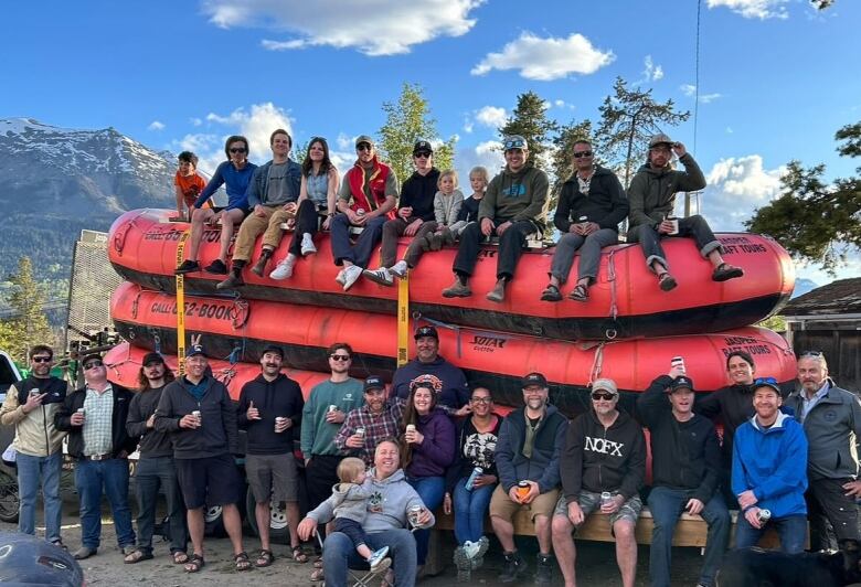 A group of people stands outside in front of a river and two large orange rafts.