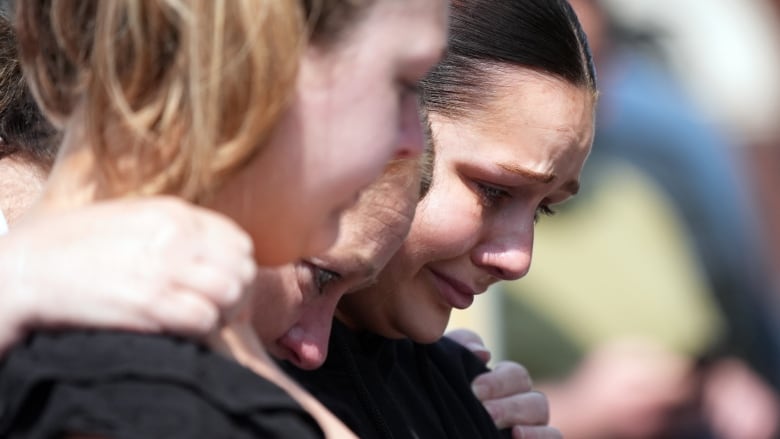 Three women shoulder to shoulder weep.