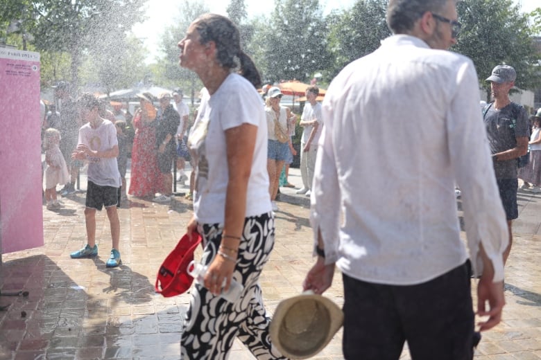 People cool themselves off next to a sprinkler 