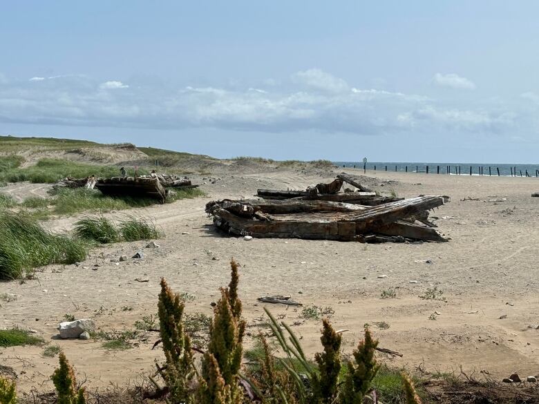 Large pieces of an old ship sit on a sandy beach.