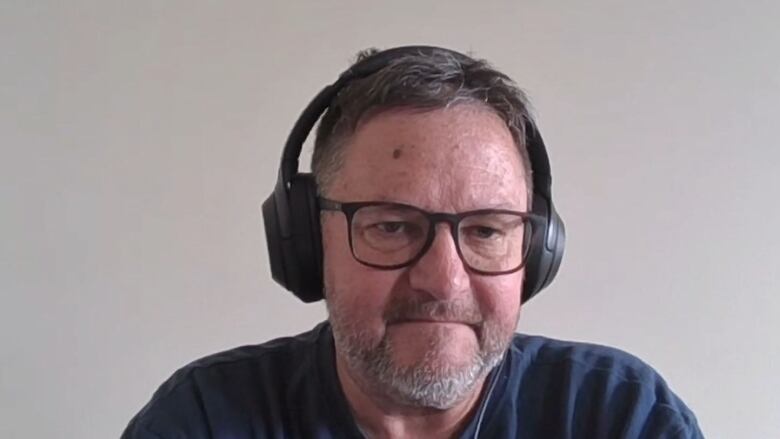 A man wearing a headset looks intensely into the camera