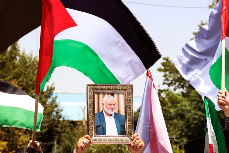 A person holds a framed photo of a bearded man near waving Palestinian flags.