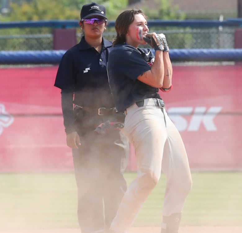 A baseball player stands at second base while an umpire looks on. 