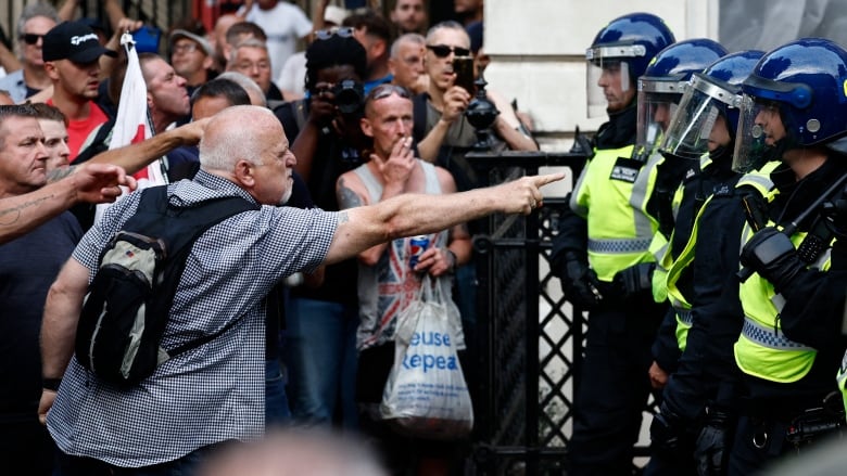 A man in a crowd points angrily at a row of police.