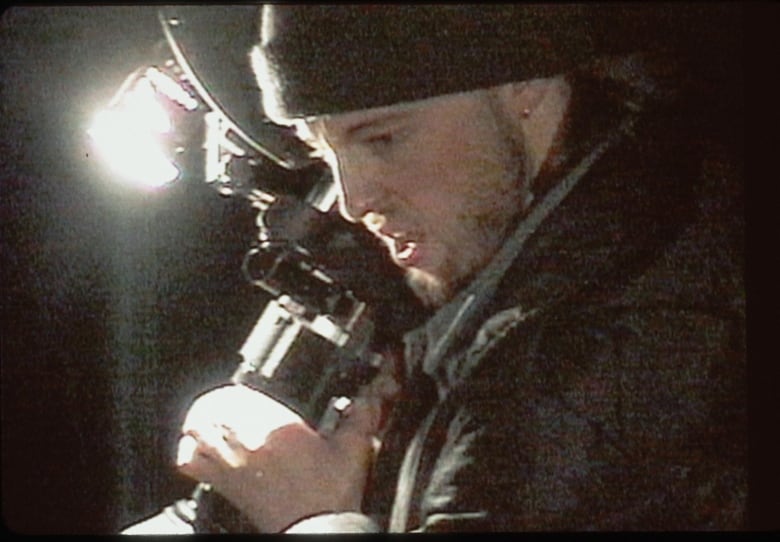 A grainy image shows a man holding a camcorder standing in the dark outside.