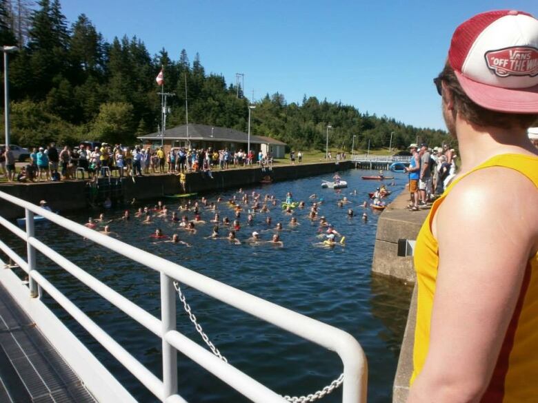 Photo shows a lifeguard in yellow at right of a large group of people in a canal.