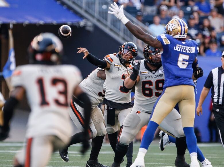 A football player in a blue and gold uniform attempts to block the opposition who throws the ball to another player on their team. 