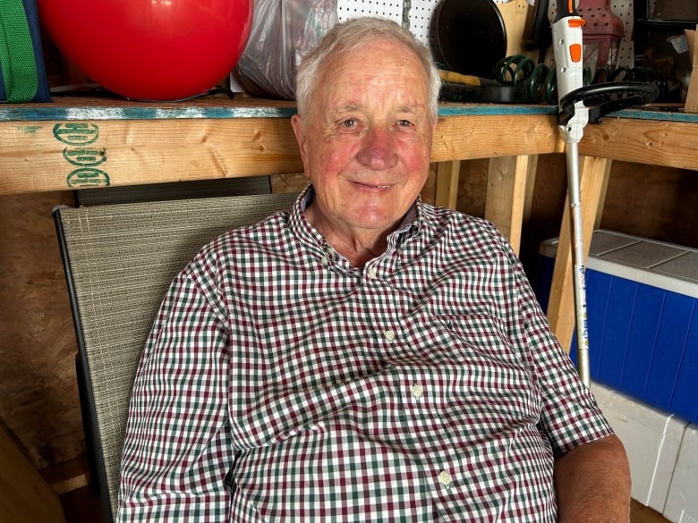 A man in a checkered shirt sits in a lawn chair in a garage.