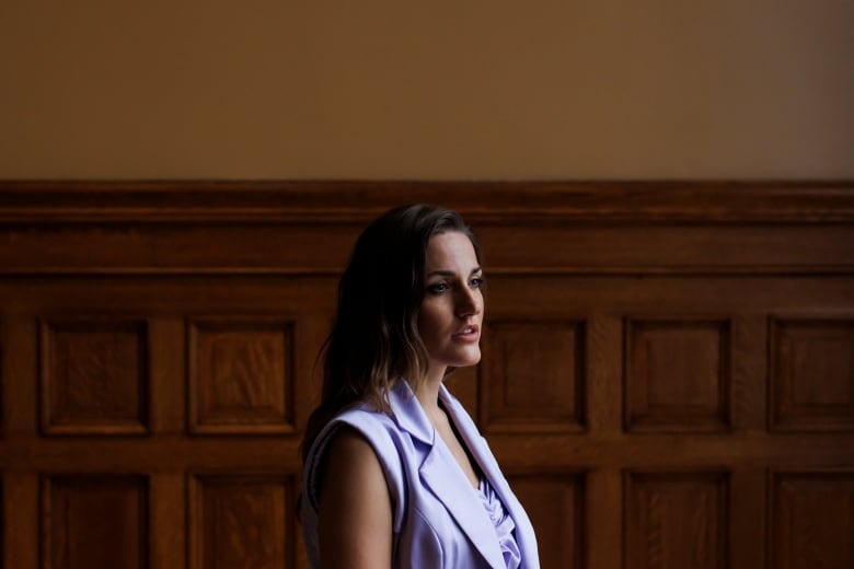 A woman is pictured in front of a wood-paneled wall.