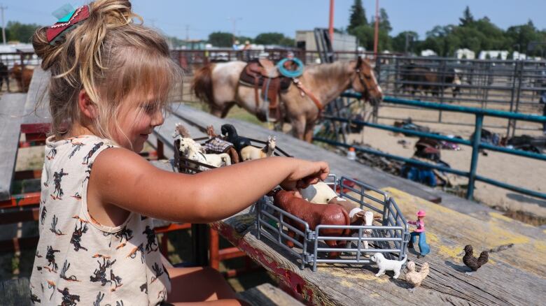 A little girl plays with a toy barnyard at a rodeo.