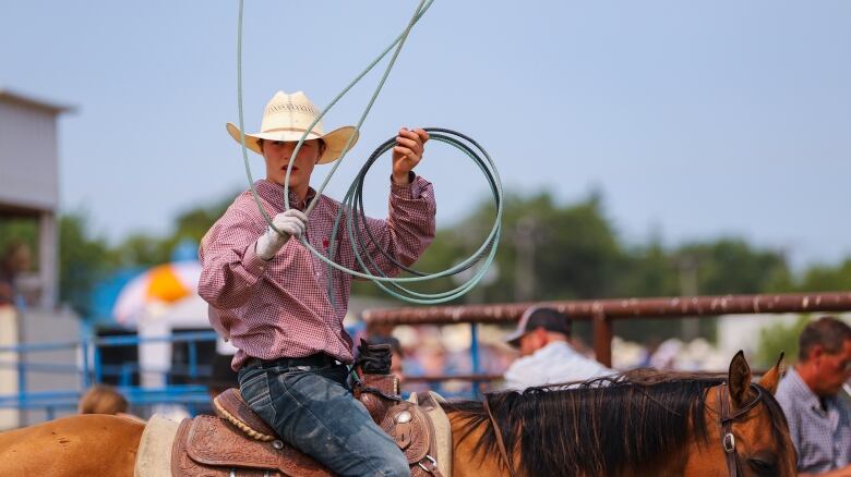 A young cowboy plays with a lassoo wihle sitting on a horse.