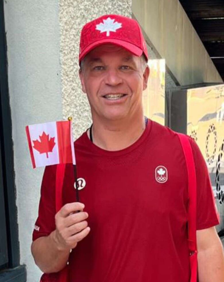 A man wearing a red shirt and red hat holding a Canadian flag. 