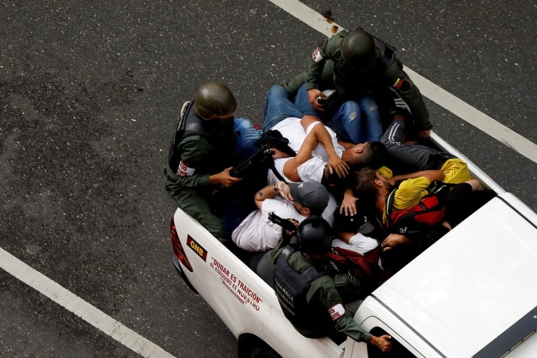 People lay in the back of a pickup truck as armed soldiers guard them.