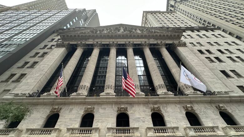 The exterior of the New York Stock Exchange building. Two American flags and an Olympic flag hang from the facade.