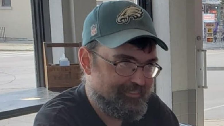 A man with a green cap, glasses, and grey beard.