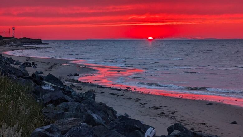 A setting sun turns the entire sky over the ocean red.