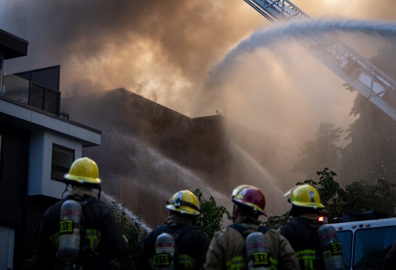 Firefighters spray water on a building shrouded in smoke.