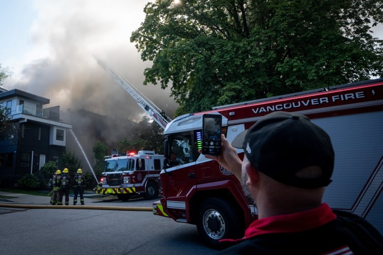 A man uses a cell phone to record firefighters extinguishing a blaze.