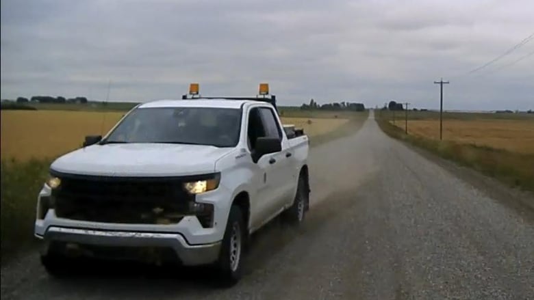 A white car drives on a gravel road. 