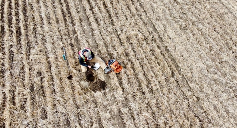 A worker sits in a field and uses soil sampling equipment