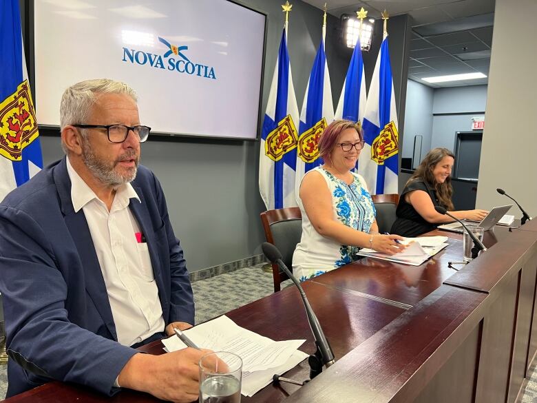 Three people sit behind a desk at a news conference