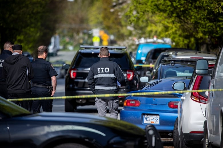 Various cars are pictured behind crime tape, with a man in the centre wearing a shirt reading 'IIO'.