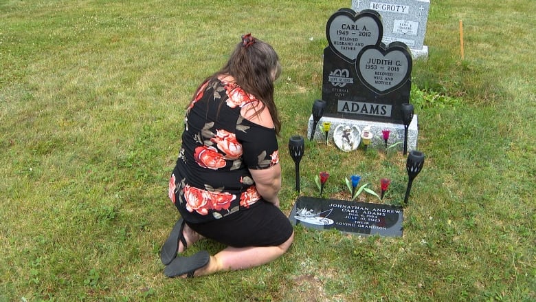 Woman kneels in front of a gravestone that's lines with solar lights. 