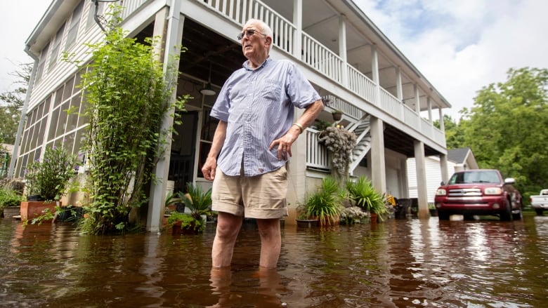 A man stands in floodwater in front of a house.