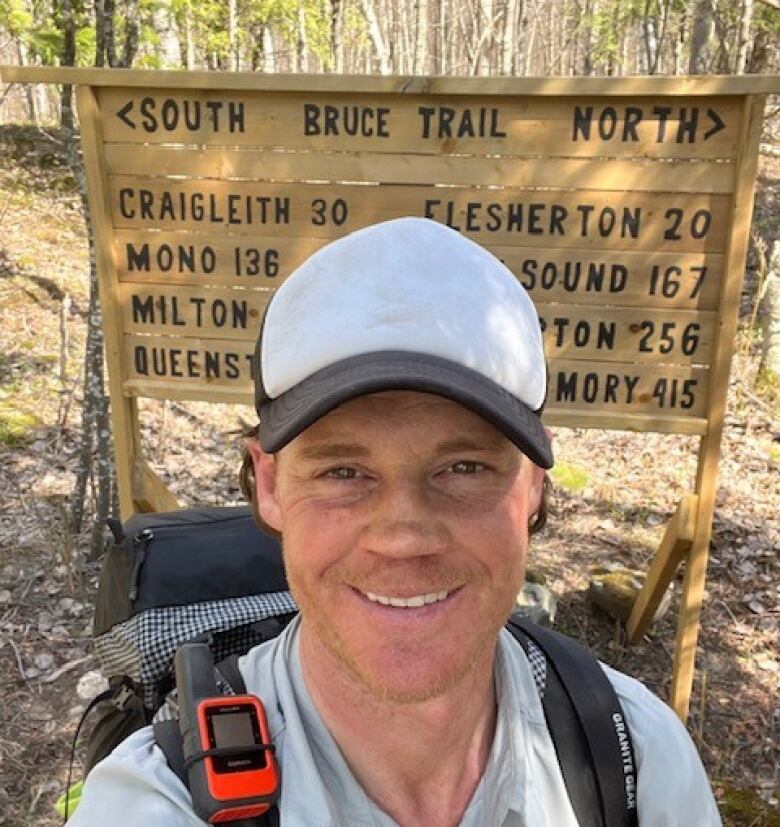 A selfie of a person in a cap and backpack posing in front of a sign marking the south Bruce Trail. 