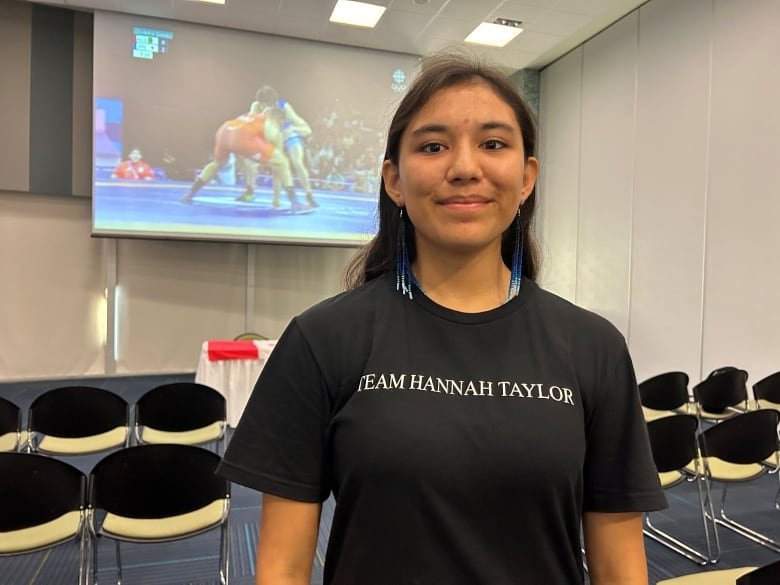 Kierra MacDougall with wrestlers on a screen in the background.