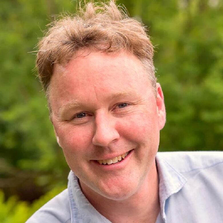 A smiling man in front of greenery