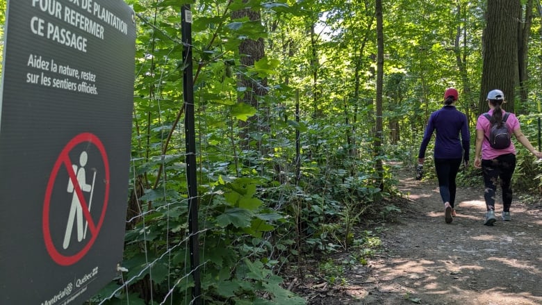 two people walking beside a fence and a sign saying not to walk 