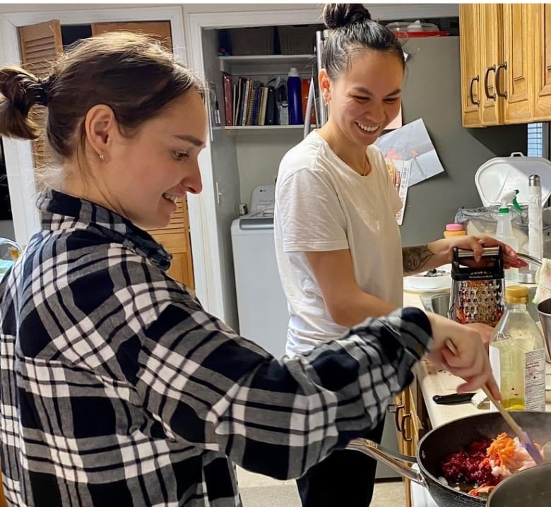 Two women stand at a stove cooking.