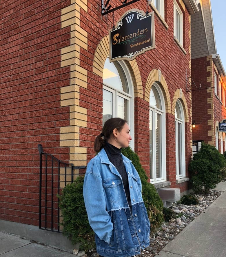 A woman stands in front of a brick building.