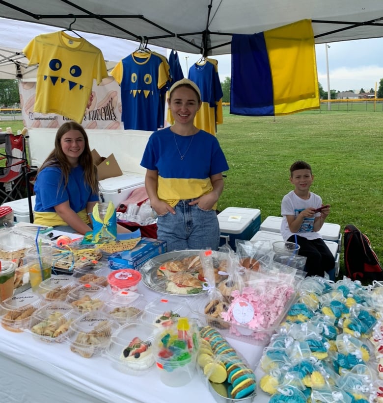 A woman wears blue and yellow in front of a stand in a field.