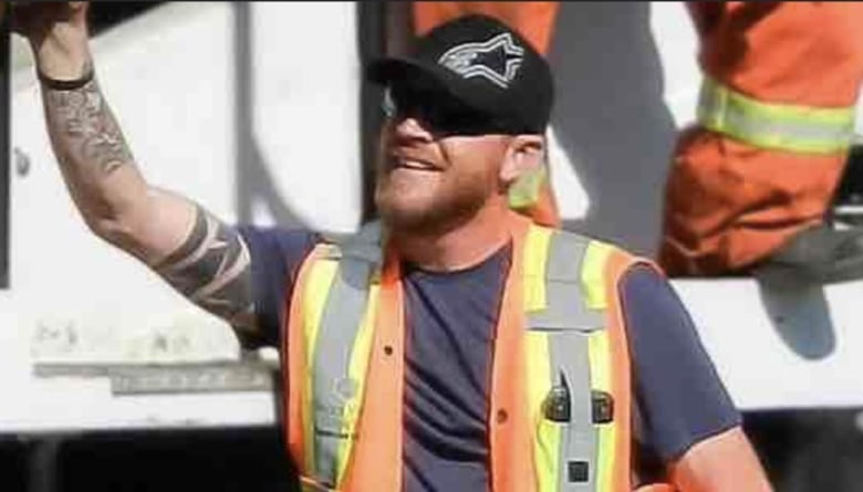 A man in an orange work vest smiles and waves. 