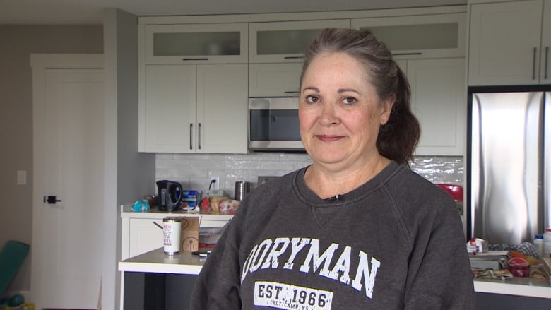 Former wildfire evacuee Helen Malone Babineau stands in her kitchen, with unopened boxes and other moving materials around her.