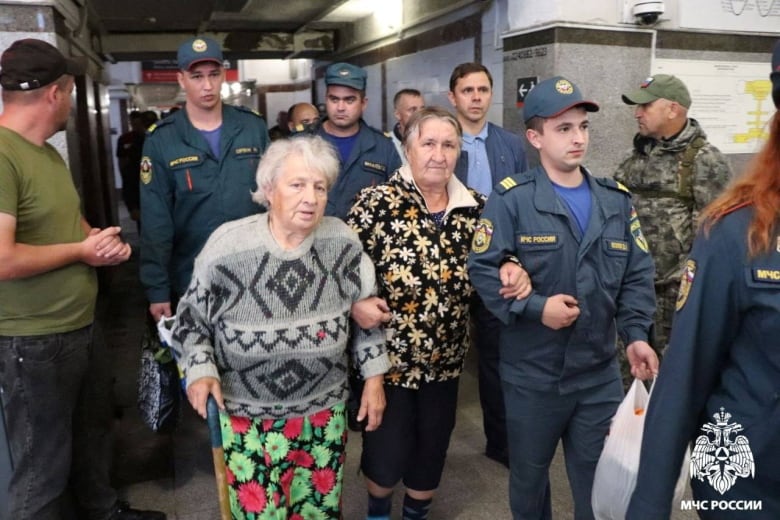 People in security uniforms escort women through a building.